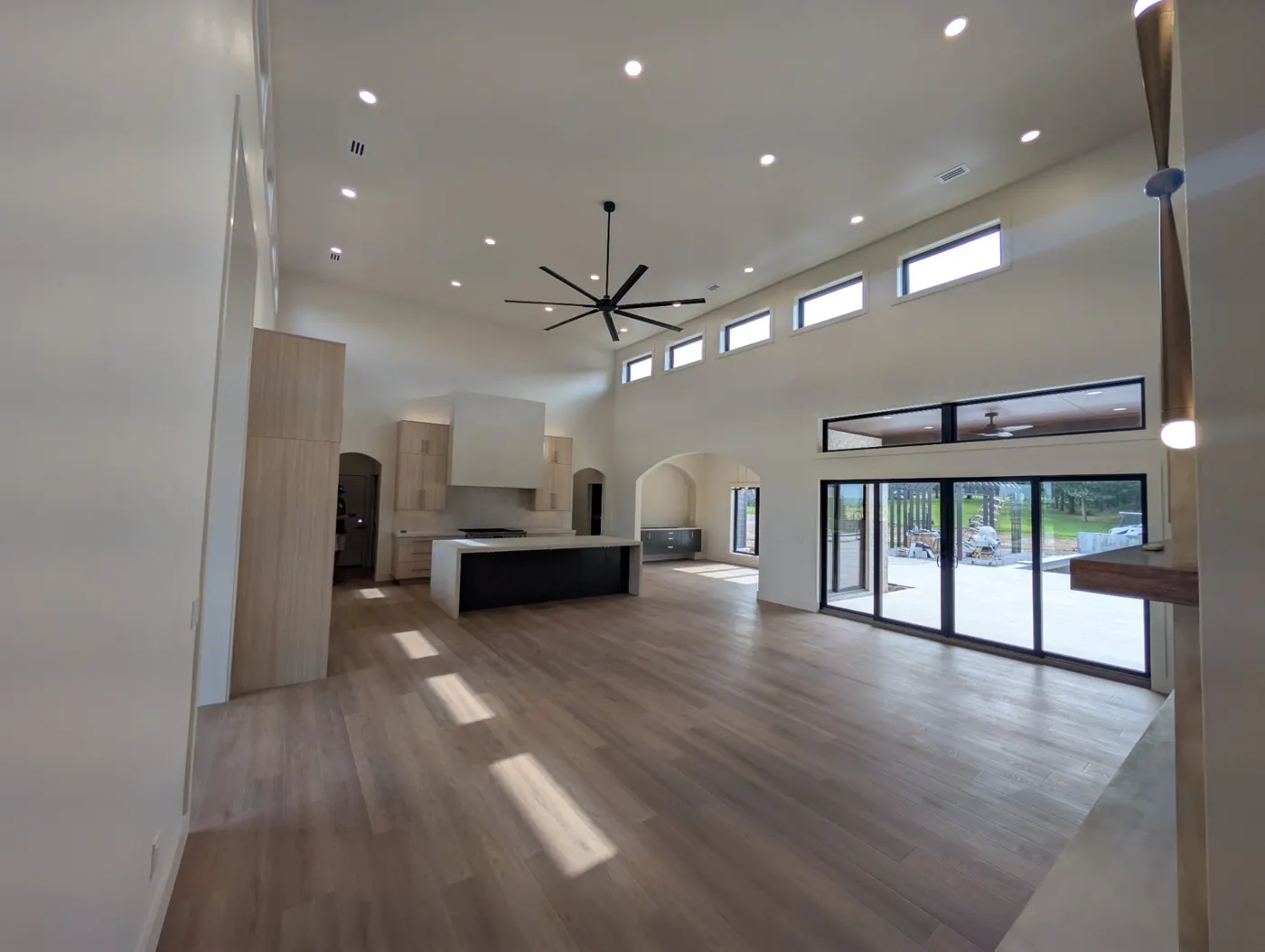 A long, bright great room in a new home with recessed lights, a black ceiling fan and a row of clerestory windows
